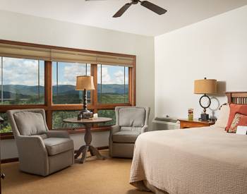 Two grey fabric chairs with a table and lamp in between, Bed has a tan bedspread